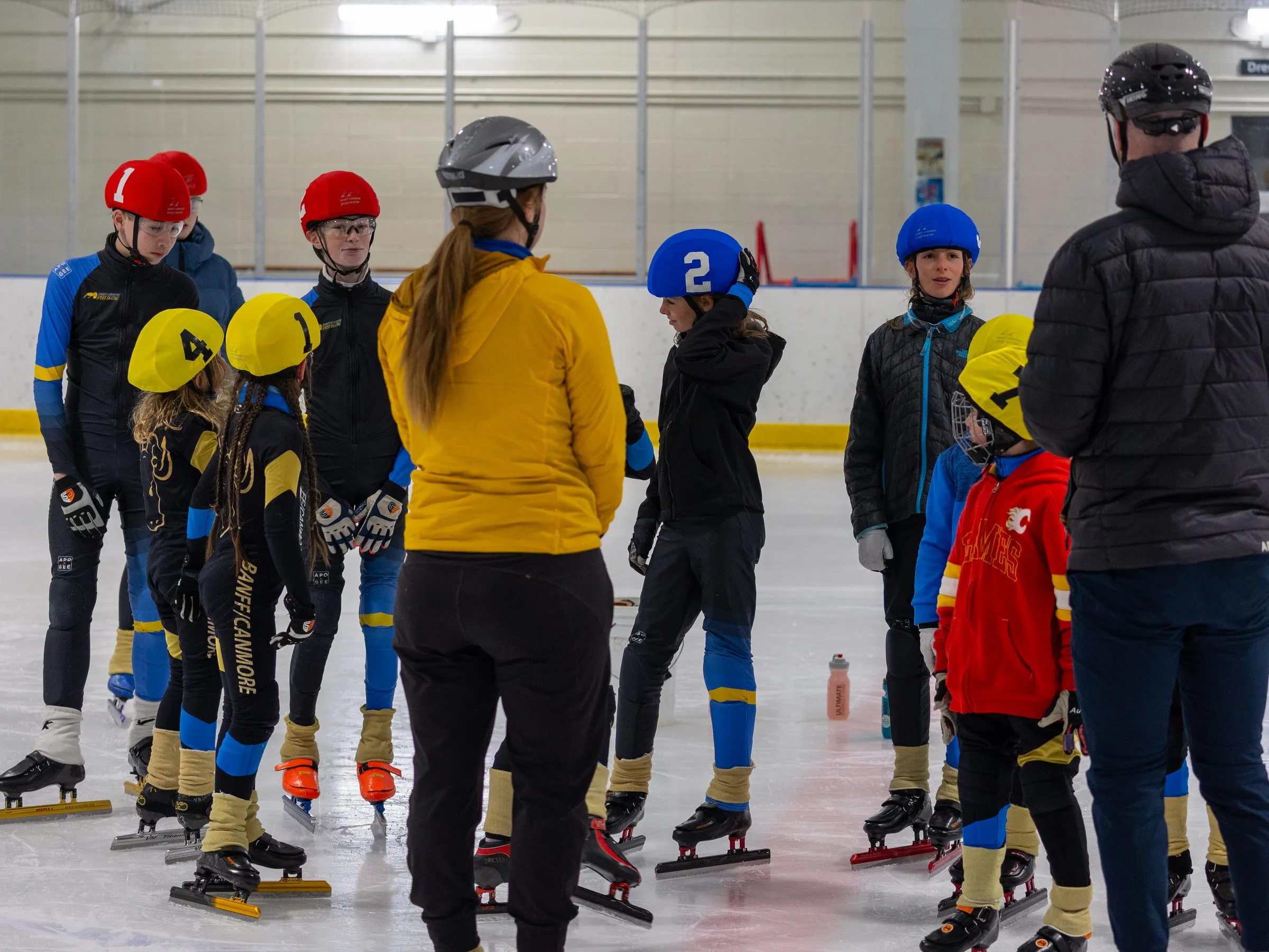 A coach talking to a group of skaters gathered on the ice