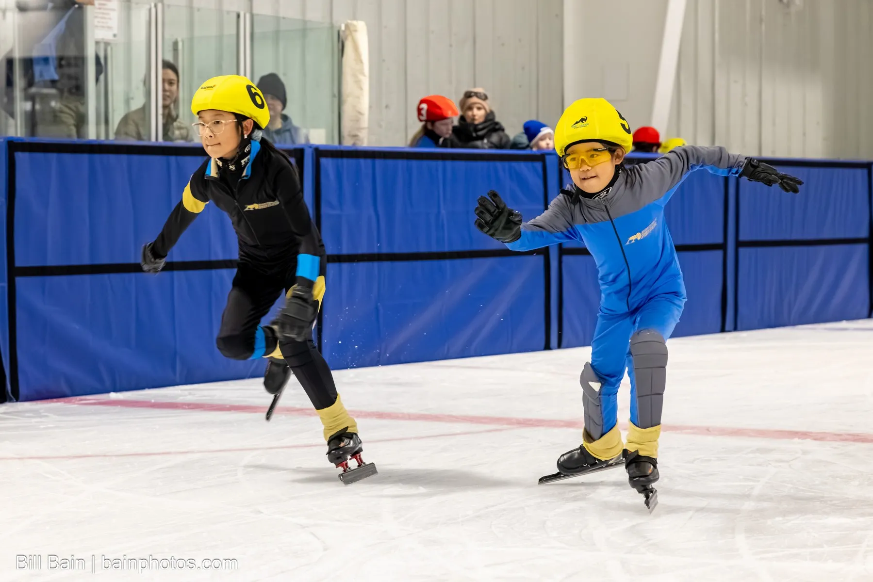 Two young skaters in yellow helmets racing side by side